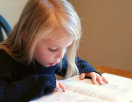 girl reading Bible. Bible memory verses for kids feature image.