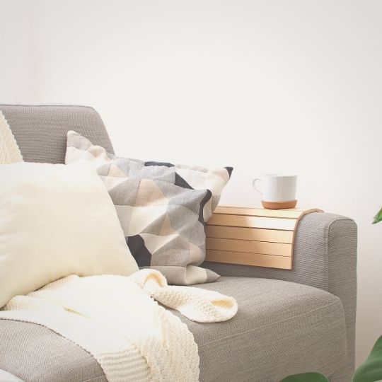 Peaceful home picture of sofa with throw blanket and pillows along with a cup of coffee on armrest table.
