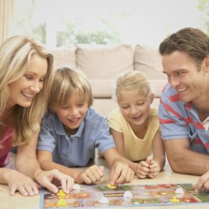 Board games for family game night feature image of family of 4 playing a game